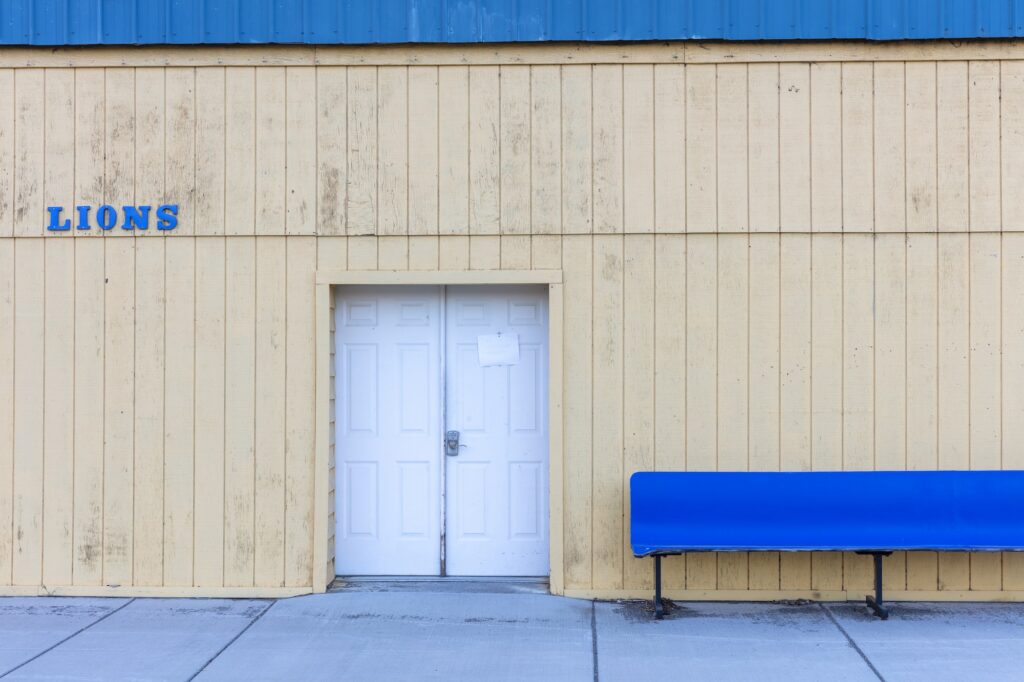 Lions Club building with the door closed and an empty blue bench outside.