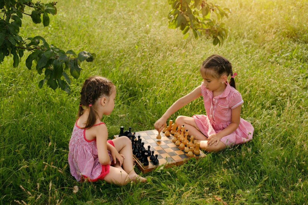Two little girls game chess in the park in nature under a tree